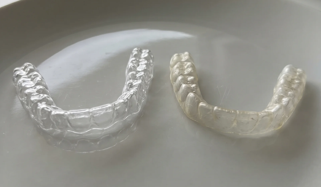 clear, clean retainer and a yellow older retainer lying flat side by side