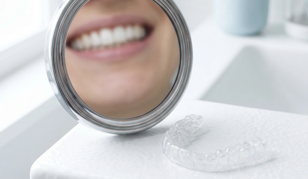 Clear retainer on a white surface beside a mirror showing straight teeth in reflection