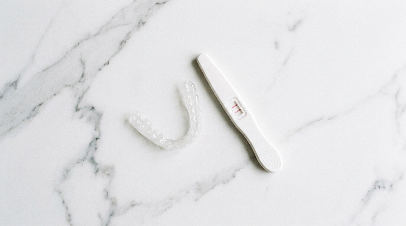 clear aligner tray beside a positive pregnancy test on white marble surface, Jawology