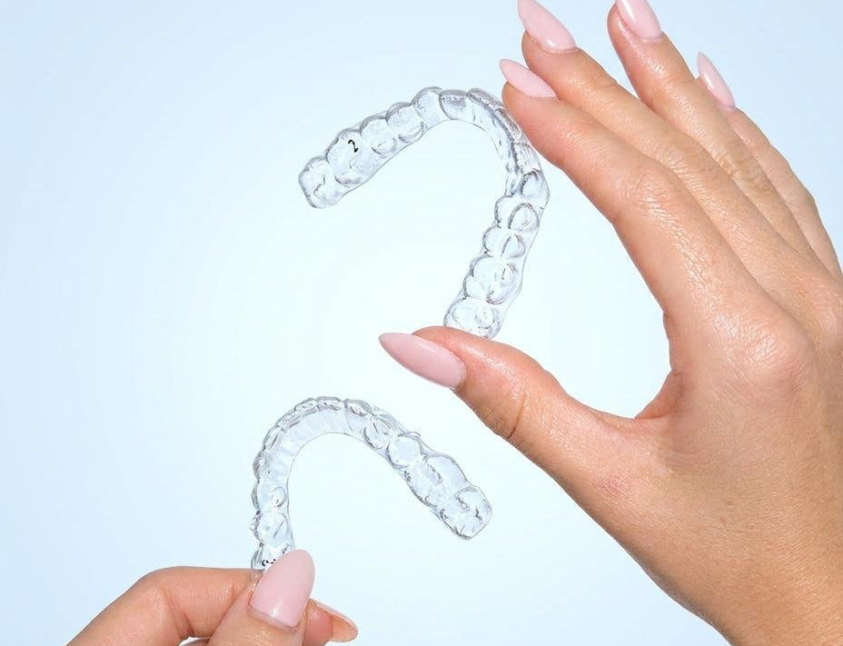 Clear dental aligners held by a hand against a light blue background